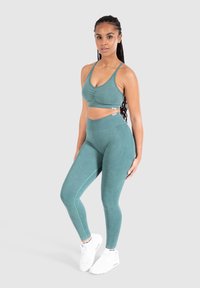 Completo sportivo turchese composto da un top corto con arricciature e leggings a vita alta. Texture liscia, dettagli laterali, abbinato a sneakers bianche.