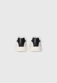 Witte sneakers met zwarte leren accenten, suede zijpanelen en getextureerde rubberen zolen. Kenmerkt zich door een strak ontwerp en handtekeningbranding op de hakken.