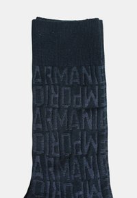 Calcetín azul marino oscuro con textura acanalada y un patrón de logotipo "ARMANI" en relieve por toda la superficie. Tela suave que ofrece comodidad y un ajuste ceñido.