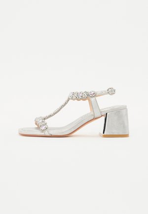Silver heeled sandal with a textured metallic finish, T-strap design, beaded embellishments, and a block heel with a metallic accent.