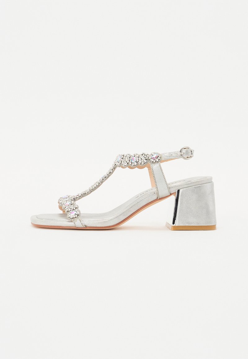 Silver heeled sandal with a textured metallic finish, T-strap design, beaded embellishments, and a block heel with a metallic accent.