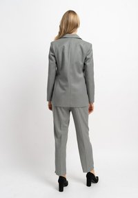 Grau maßgeschneiderter Anzug mit einem strukturierten Blazer und schmal geschnittenen Hosen. Entworfen aus glattem Stoff und mit einem klassischen Revers, kombiniert mit schwarzen High Heels.