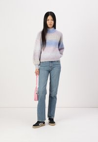 Maglione con gradienti pastello in morbido tessuto, abbinato a jeans a gamba dritta blu chiaro e sneakers nere con dettagli bianchi. Tieni in mano una borsa rosa.