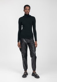 Maglione nero a coste con collo arricciato, abbinato a pantaloni cargo neri in ecopelle con tasche laterali e polsini elastici.