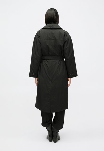 Dlhý čierny kabát s pásom v páse, oversize golierom a manžetami na gombíky. Hladká textúra a strih do výšky kolien.