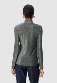 Top lucido grigio scuro a maniche lunghe con collo alto, caratterizzato da una texture liscia e un design aderente, abbinato a pantaloni in denim scuro.