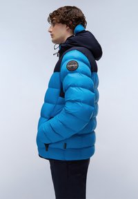 Giacca imbottita blu e navy con cappucci, dotata di un distintivo sulla spalla, tasche laterali con zip e un design trapuntato.