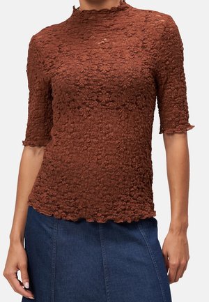 Braunes, strukturiertes Spitzentop mit kurzen Ärmeln und welligen Kanten, getragen zu einem blauen Jeansrock, gezeigt von den Schultern bis zu den Hüften.