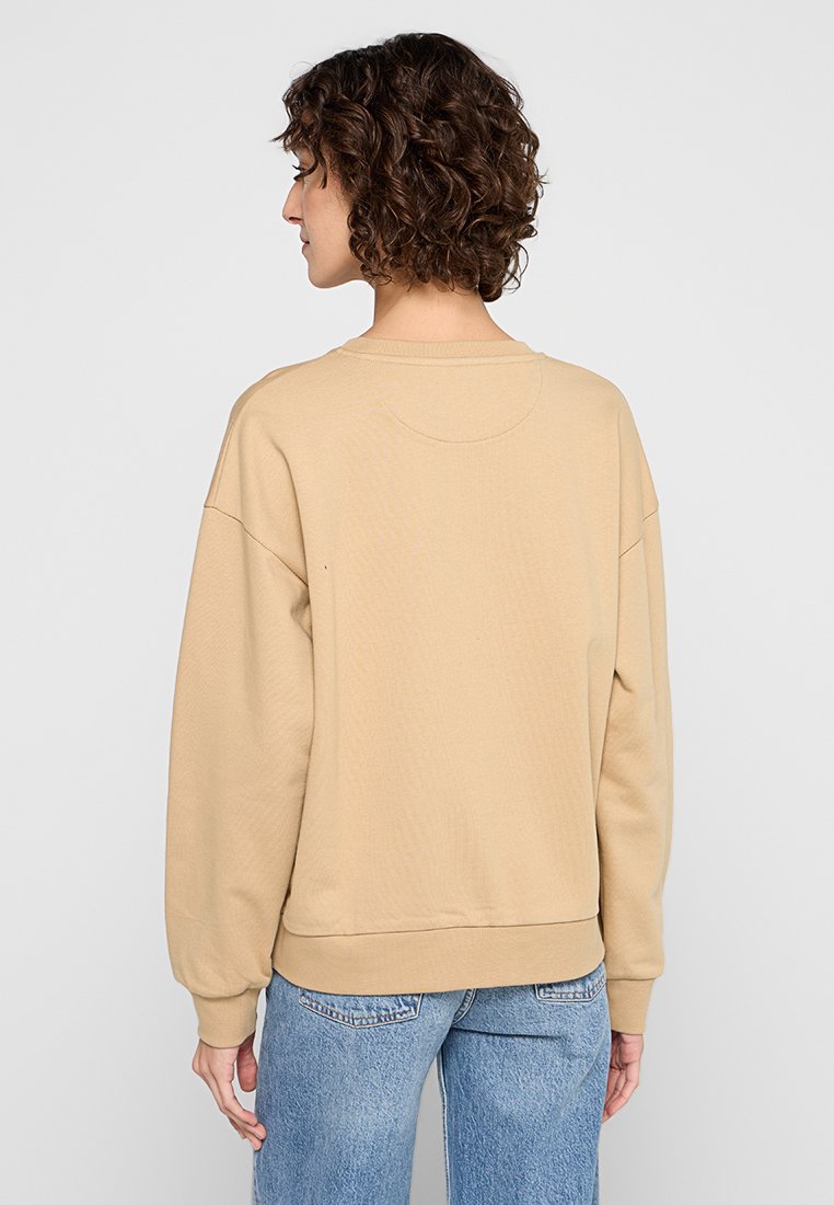 Sudadera beige con un corte relajado, puños y dobladillo acanalados. Presenta un escote redondo y una tela suave y texturizada. Se muestra vista trasera.