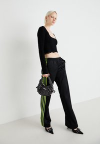 Melnas garas piedurknes blūze ar savilktu tekstūru, melnas bikses ar neona zaļām sānu svītrām, melnas norādītu pirkstu augstpapēžu kurpes un ar pērlītēm rotāta melna rokassomiņa.