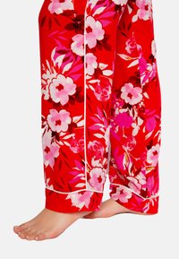 Rode pyjamabroek met een bloemenpatroon in roze en wit, voorzien van witte bies langs de naden. De stof lijkt zacht en lichtgewicht te zijn.