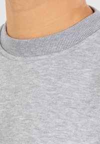 Col en sweat gris avec texture côtelée ; le tissu est doux et légèrement chiné, montrant une surface lisse avec un minimum de détails.