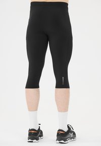 Svarta tights med en slät textur, längd till mitt på vaden och reflekterande detaljer på sidorna. Kombineras med svarta träningsskor och vita strumpor.