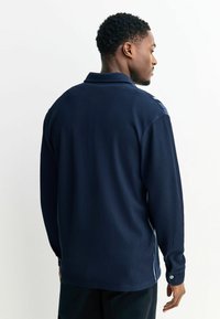 Jūrininkų ilgarankovė marškiniai su vertikaliu raukšlėtu audiniu, užsegamos tamprėmis, su smailiu apykakle ir šoniniais plyšiais apačioje.