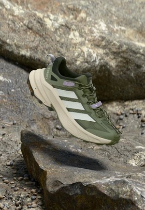 Groene buitenschoen met een structuur van mesh bovenwerk, witte strepen en een beige rubberen zool. Voorzien van een stevig vetersysteem en een verstevigd teenstuk.