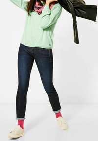 Mátově zelená košile s dlouhým rukávem, tmavé džíny skinny, ohrnuté rukávy, růžové ponožky a bílé tenisky. Šála má růžový a černý vzor.