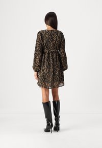 Žena v černých a hnědých pruhovaných šatech se dlouhými rukávy, stojící zády k fotoaparátu, v kombinaci s černými vysokými kozačkami na podpatku.