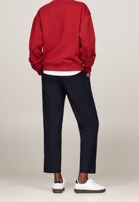 Rode sweatshirt, marineblauwe broek en witte sneakers. De sweater heeft een relaxed fit met geribde manchetten; de broek is recht met zijzakken.