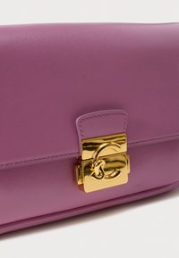 Μωβ δερμάτινο τσαντάκι χειρός με χρυσό κούμπωμα λογότυπου, δομημένο σχήμα και εμφανείς ραφές στην κορυφή κατά μήκος των ακρών.