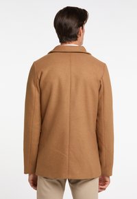 Palton din lână maro cu un design croit pe măsură, ventrală unică la spate și guler cu colțuri. Textură netedă, mâneci lungi și siluetă dreptă.