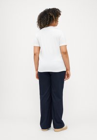 Λευκό κοντομάνικο μπλουζάκι με στρογγυλή λαιμόκοψη, συνδυασμένο με σκούρες ναυτικές παντελόνες φαρδιές και ανοιχτόχρωμα υποδήματα.