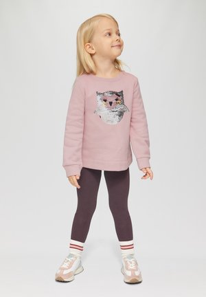 Sweatshirt rose clair avec un motif de hibou en sequins, associé à des leggings violets foncés et des chaussettes rayées rouge et blanche. Baskets avec des accents pastel.