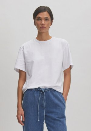 T-shirt en coton blanc à manches courtes et col rond, associé à un pantalon en denim bleu clair avec cordon de serrage. Coupé simple et décontracté.