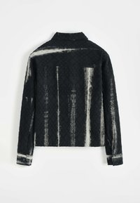 Veste noire texturée avec un motif en losanges et des rayures blanches, manches longues, col et boutons aux poignets.