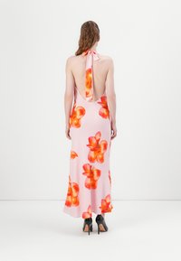 Bakfra av en rosa blomsterkjole med store oransje blomster, halterneck-bind, og åpen rygg, sammen med svarte høye hæler. Glatt stoff.