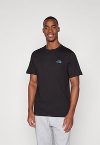 Camiseta de algodón negra con un logo turquesa de The North Face en el pecho. Mangas cortas y un cuello redondo clásico.