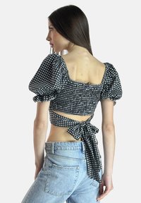 Schwarz-weißer karierter Puffärmel-Oberteil mit gerafftem Mieder, offener Rückseite und Schleifendetail an der Taille, kombiniert mit hoch taillierten Jeans.