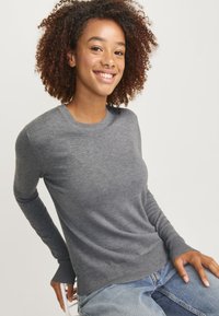 Grau, langärmliger Pullover mit Rundhalsausschnitt, aus weichem Material. Gerippte Ärmelbündchen und Saum, taillierte Passform, getragen mit Jeans.