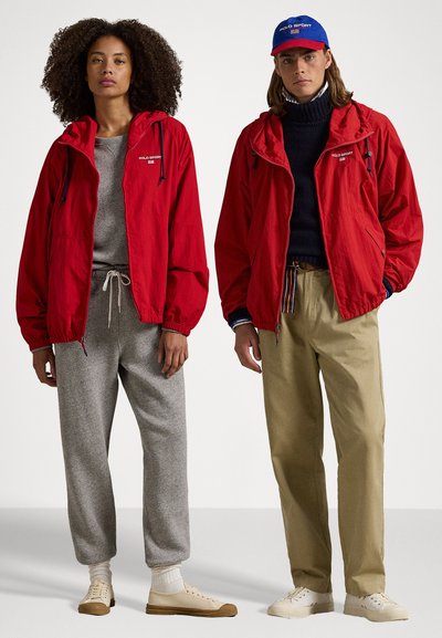 Κόκκινες κουκούλες, γκρίζες φόρμες, μπεζ τζιν; η πρώτη εμφάνιση περιλαμβάνει αθλητικά παπούτσια και η δεύτερη περιλαμβάνει ένα μπλε καπέλο με λογότυπο.