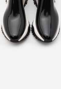 Baskets en cuir verni noir avec une semelle intermédiaire blanche, une semelle extérieure en caoutchouc noir texturé et un design à bout rond. Présente des accents minimalistes.