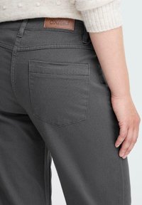 Personer som har på seg mørkegrå jeans med baklomme og et skinnmerke fra oxmo på livbåndet, hånden hvilende ved siden av.