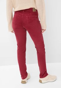 Pantalons en velours côtelé rouge à coupe slim, avec deux poches arrière et une ceinture simple, associés à des sneakers de couleur claire.