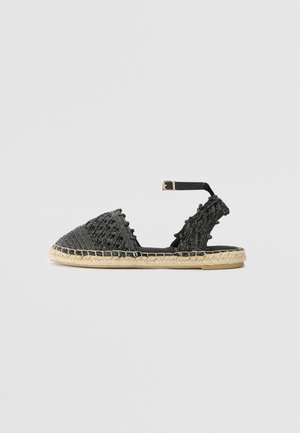 Sandale plate espadrille noire tissée avec bride à la cheville et boucle, dotée d'une semelle en jute naturelle et de détails texturés sur les zones des orteils et du talon.