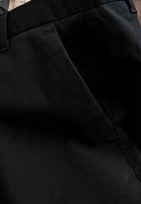 Lähikuva mustasta kangasvaatteesta, jossa näkyy sivutasku ompeleineen ja taitettu vyötärönauha.