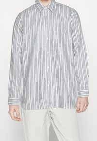 Witte overhemd met verticale blauwe strepen, lange mouwen, een borstzak en een ronde zoom. De stof heeft een gladde textuur.