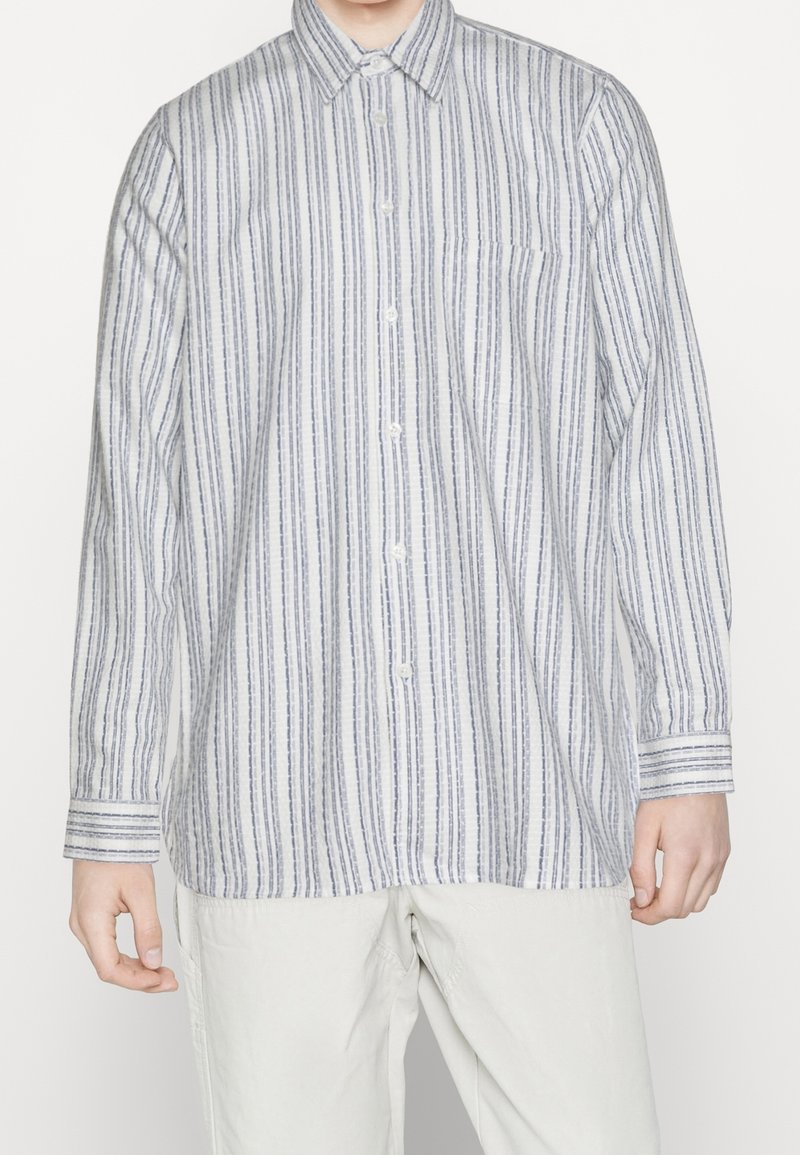 Witte overhemd met verticale blauwe strepen, lange mouwen, een borstzak en een ronde zoom. De stof heeft een gladde textuur.
