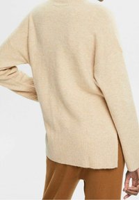 Beige gebreid sweater met een hoge kraag, brede mouwen en geribbelde zoom. De stof lijkt zacht met een iets gestructureerde afwerking.