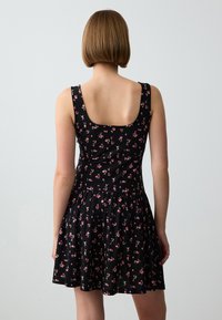 Zwart mouwloos jurkje met een getailleerde bovenkant en een flared rok; beschikt over een bloemenprint in roze en groen, zachte stof en een vierkante halslijn aan de achterkant.