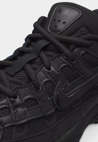 Κοντινή λήψη μαύρου αθλητικού παπουτσιού Nike με ύφασμα από δίχτυ, υφασμάτινες επενδύσεις με υφή, κορδόνια και λογότυπα της μάρκας στη γλώσσα και στα πλευρά.