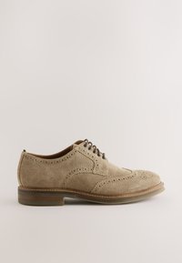Chaussure brogue en daim marron clair avec design à bout ailé, détails perforés, lacets marron et talon empilé bas sur fond neutre.