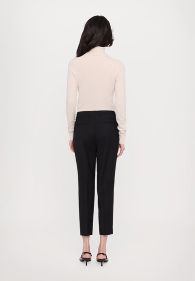 Light beige turtleneck sweater with long sleeves, fitted design. Paired with black tailored trousers and black strappy heeled sandals.