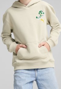 Felpa beige con cappuccio e tasca frontale, decorata con un logo verde e bianco con accenti gialli. Materiale morbido con polsini a costine.