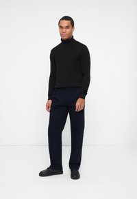 Maglione nero a collo alto con lavorazione a maglia, abbinato a pantaloni blu navy e scarpe nere. Design semplice e silhouette aderente.