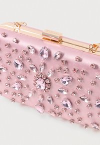 Růžová saténová kabelka s zlatým kováním, zdobená uspořádáním různých velikostí růžových kamínků a centrálním květinovým designem.