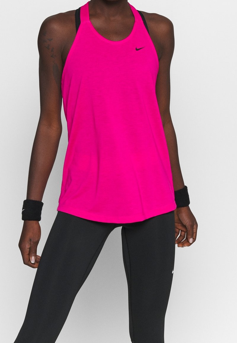 Athlète portant un débardeur de sport rose vif avec des bordures noires, des leggings noirs et des bracelets noirs, debout devant un fond uni.