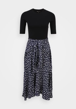 Sort kortærmet tætsiddende top kombineret med en højtaljet, navyblå midi-nederdel med et hvidt abstrakt mønster og bindedetalje foran.